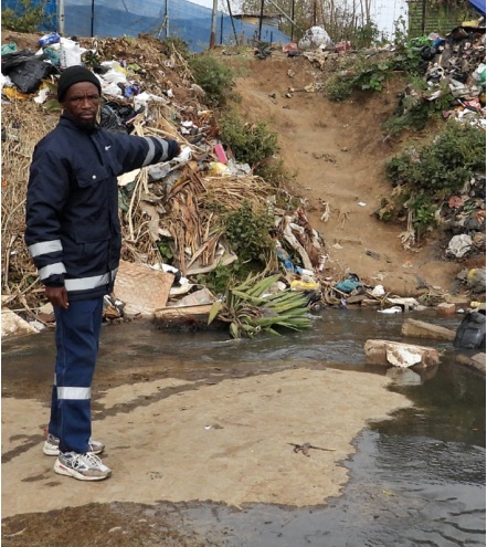 Community member Jones Mpansqhiso points out accumulated rubbish and water at the crossing. During heavy rain, residents say the route can become extremely dangerous and at times impossible to use.