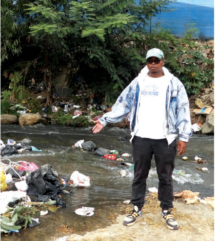 Community representative Avuyile Mabhunguza stands amid waste and dirty water at the crossing used by residents to reach schools, workplaces and essential services.